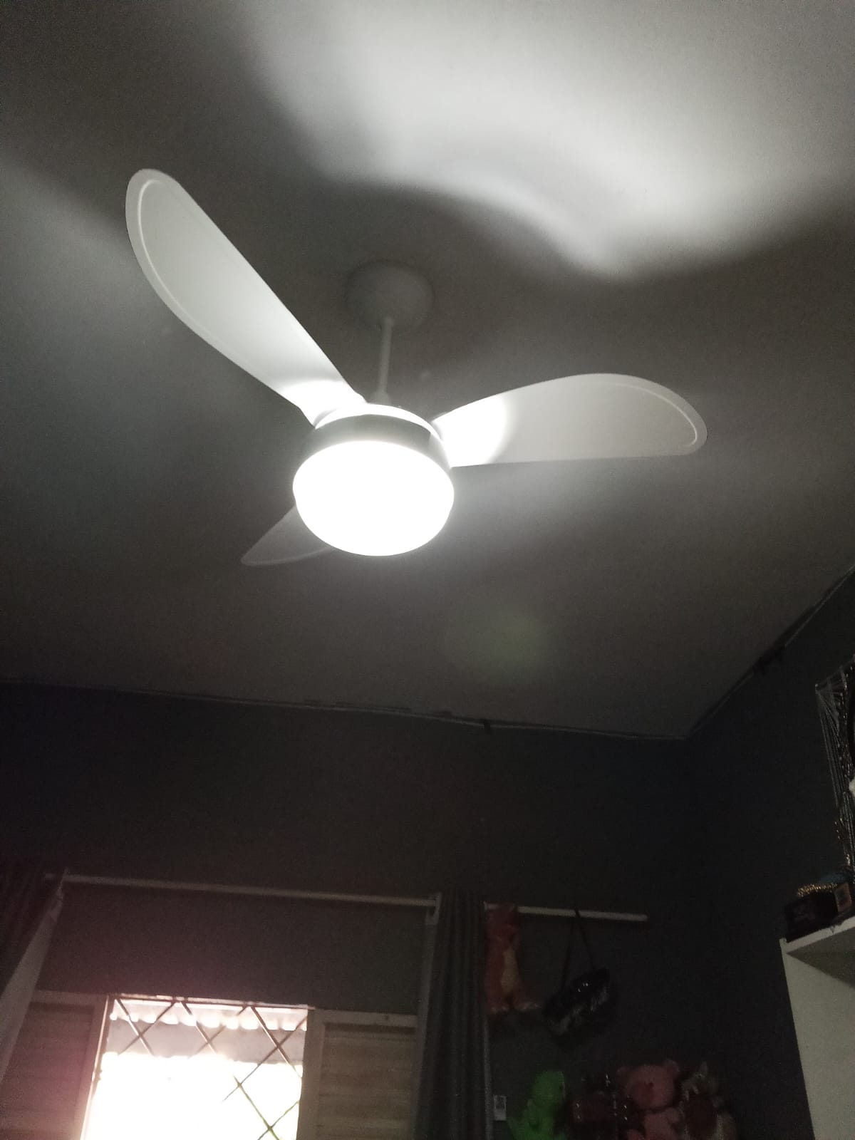 ventilador de teto branco de três pás com luminária de LED acesa instalado num ambiente interno com janela ao 