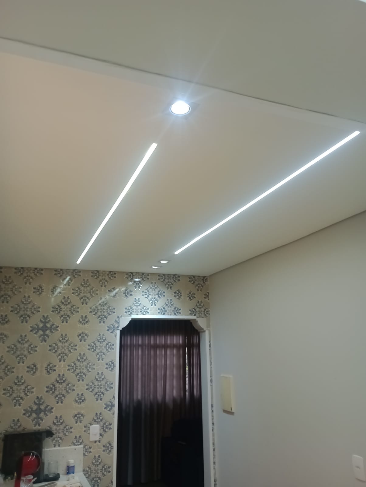 sancas de gesso com iluminação em LED embutida no teto de uma residência, com papel de parede e cortina ao fun