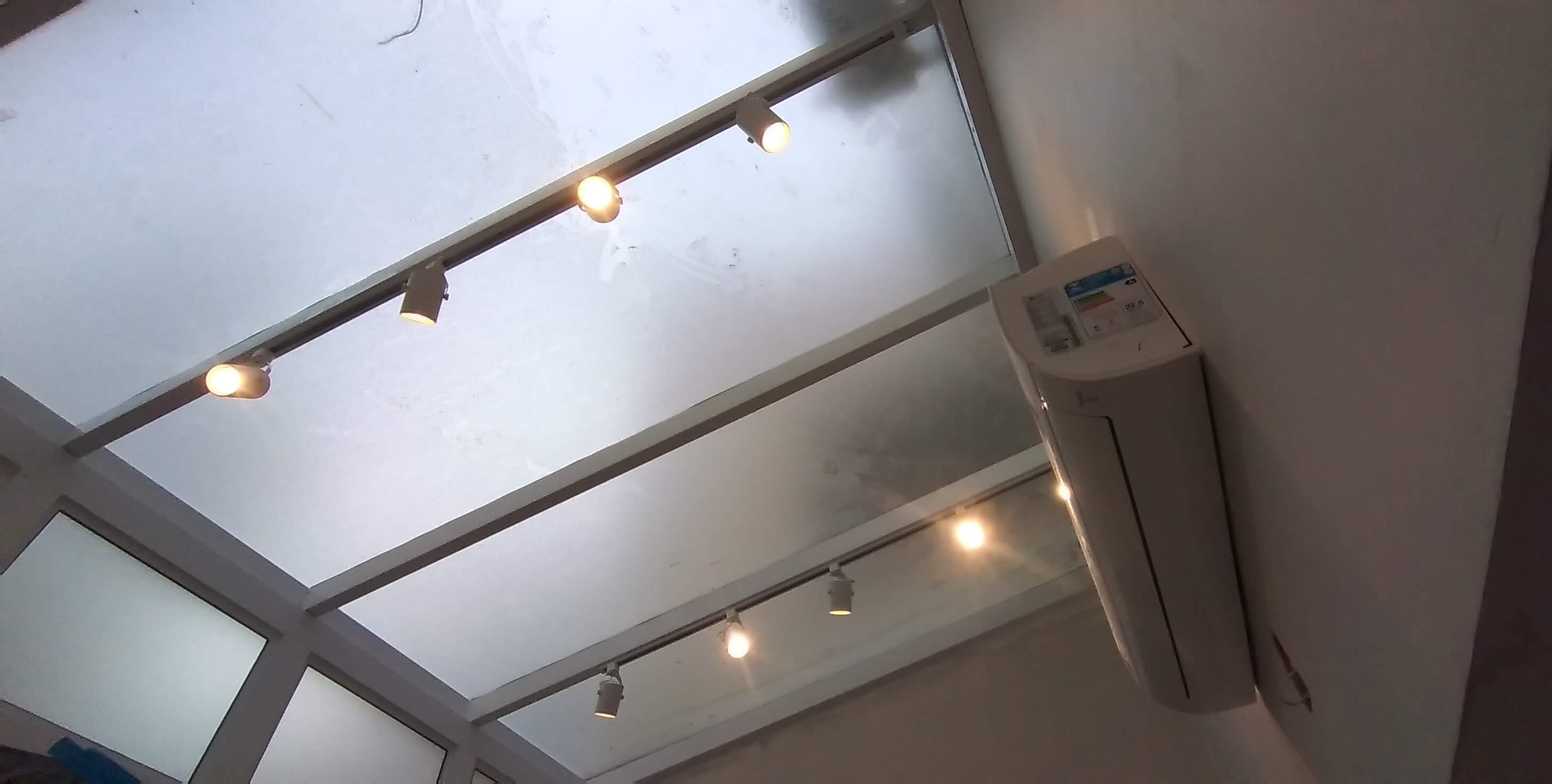 teto de vidro branco de um ambiente com trilhos de spots acesos e um ar-condicionado split LG instalado na par