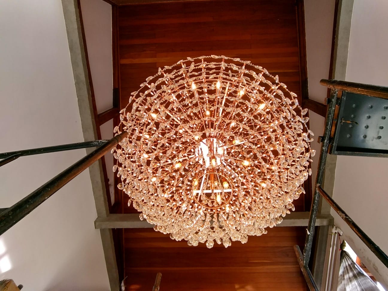 lustre de cristal grande e aceso visto de baixo, instalado em teto de madeira, com andaimes ao redor