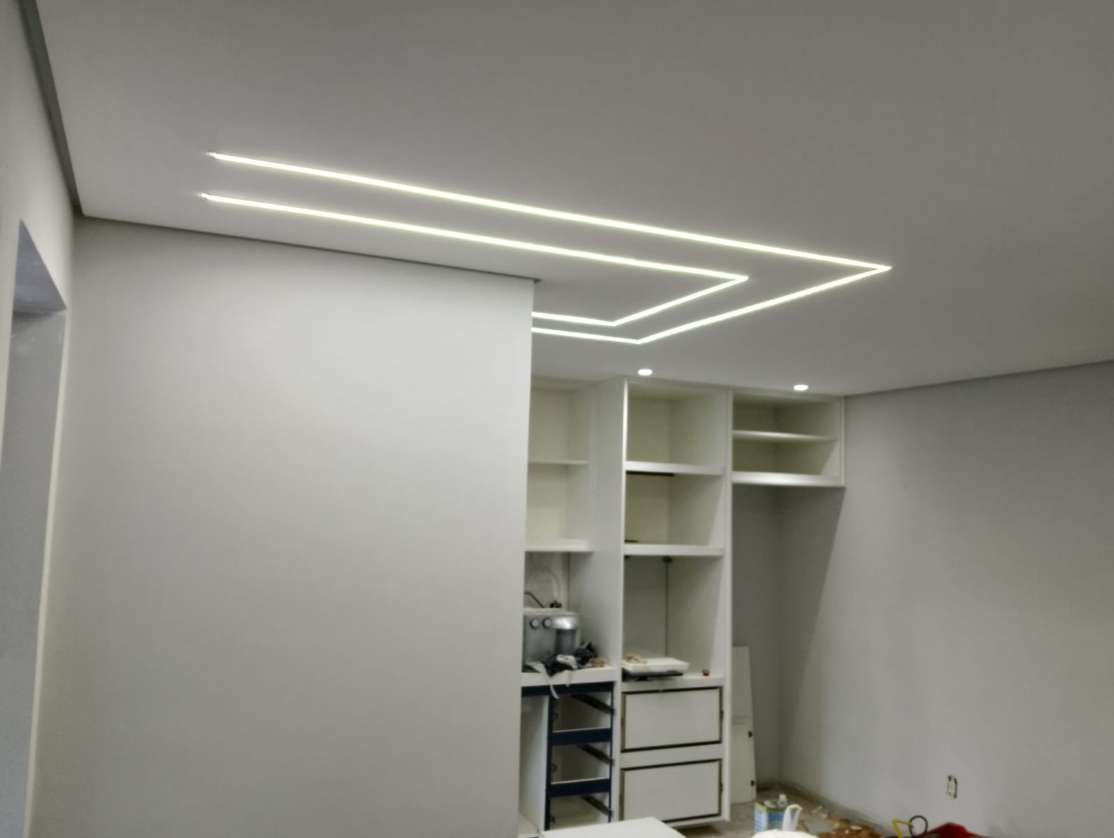 sala em reforma com sancas de gesso e fita de LED no teto formando traços retangulares, ao lado de um armário 
