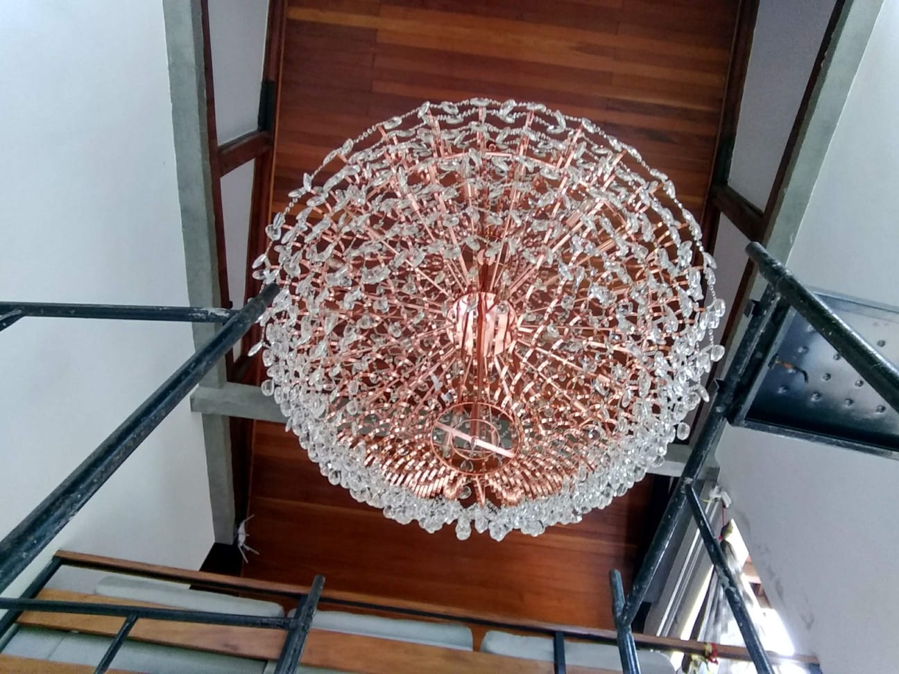 lustre grande de cristal com estrutura dourada visto de baixo, instalado no teto de madeira de uma escada, com