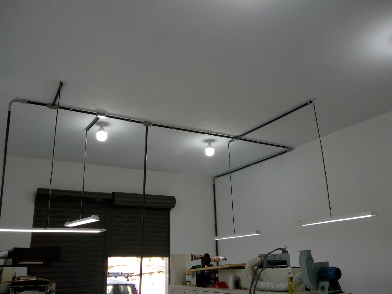 instalação elétrica com conduítes pretos no teto e luminárias LED pendentes em uma oficina